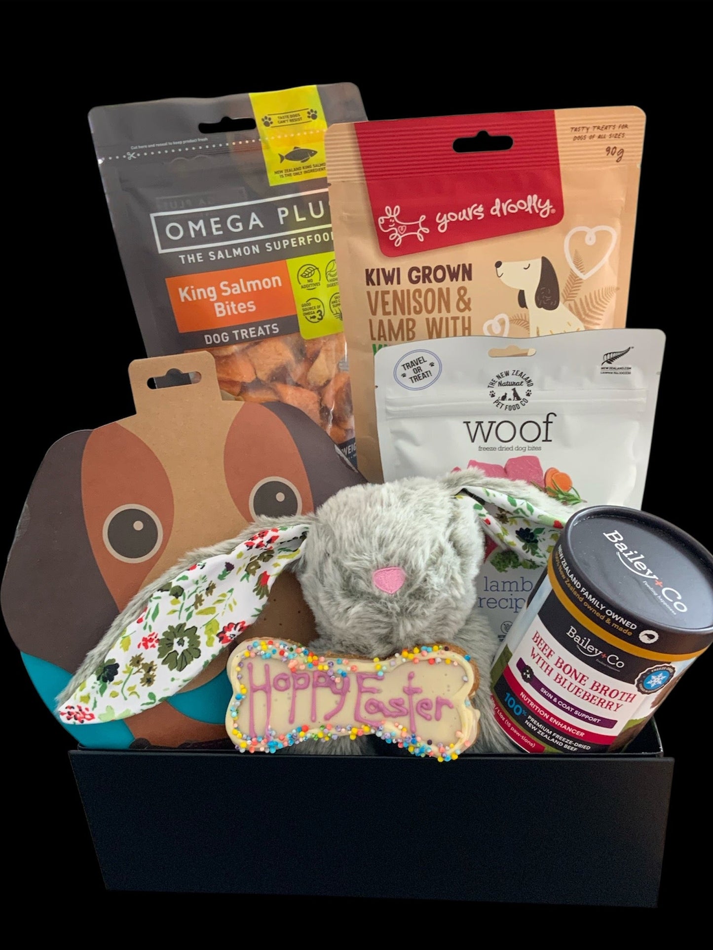 Dog gift basket with various treats and toys on a black background